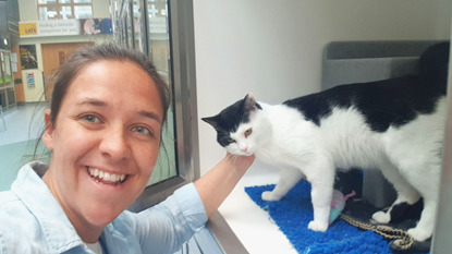 brunette woman stroking behind the ear of a black and white cat in Cats Protection adoption centre