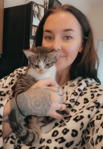 long-haired brunette woman wearing leopard print dressing gown and holding tabby-and-white kitten