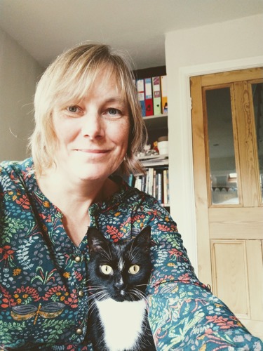 blonde-haired woman wearing floral shirt with black-and-white cat sat in front of her