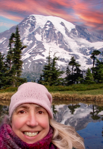 woman with long blonde hair wearing pink woolly hat in front of fake backdrop of snowy mountain