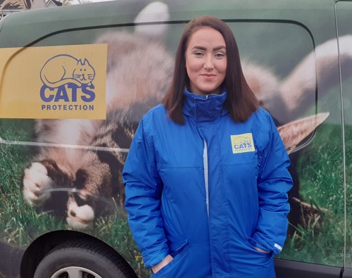 woman with long brunette hair wearing blue rain mac with Cats Protection logo standing in front of van with Cats Protection logo on the side