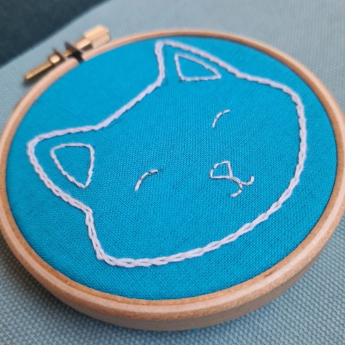 outline of a cat's face made with chain stitch on blue fabric in an embroidery hoop