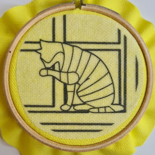 outline of a stiped cat licking its paw on yellow fabric in an embroidery hoop