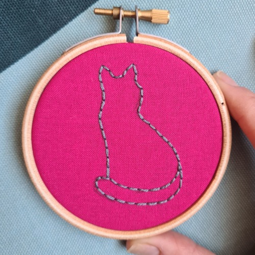 outline of a cat made with back stitch on pink fabric in an embroidery hoop