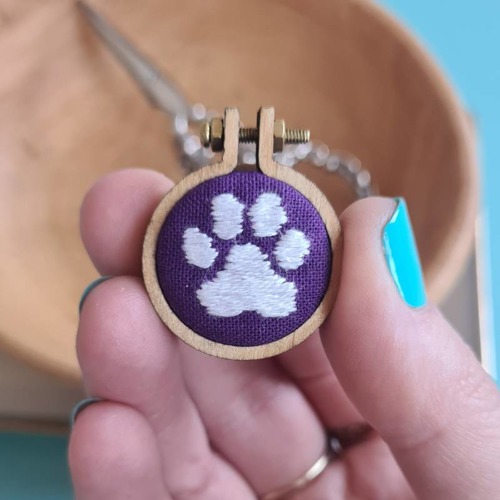 white paw print sewn with satin stitch on purple fabric in small embroidery hoop