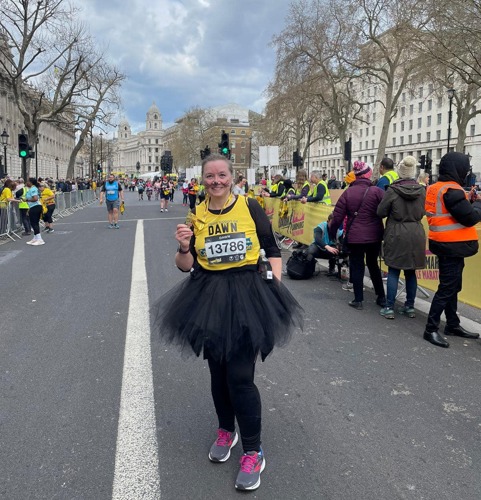 Woman on road wearing yellow Cats Protection-branded running vest , black tutu shirt and  black cat ears headband holding medal
