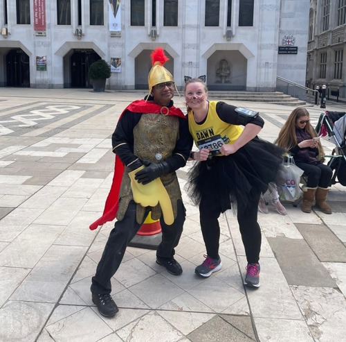 woman wearing yellow Cats Protection branded running vest, black tutu shirt and black cat ears headband standing next to man dressed as Roman warrior