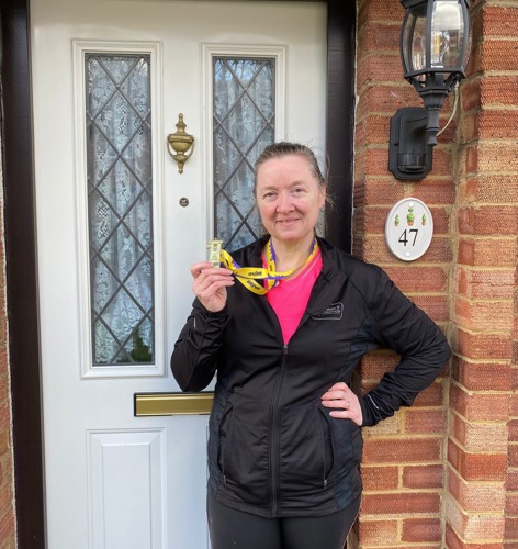 woman standing in front of white door wearing black running clothes and holding medal