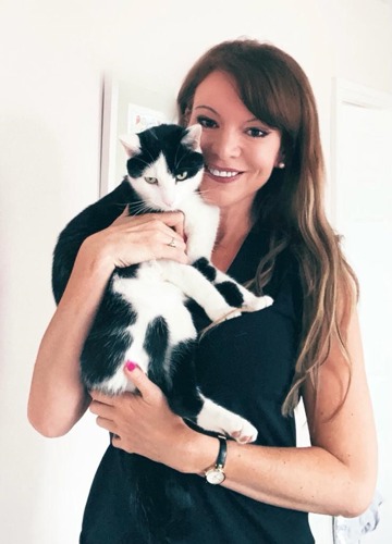 woman with long brunette hair wearing black dress holding  black-and-white cat