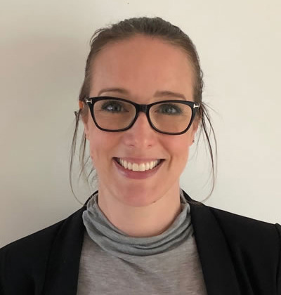 woman with brown hair tied back and black glasses wearing grey top and black jacket