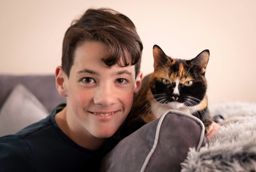 young boy with short brown hair next sat next to tortoiseshell cat