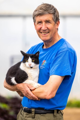 man with short grey hair and blue t-shirt holding black-and-white cat