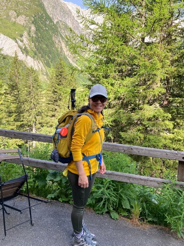 Woman wearing yellow top, white cap and hiking backpack with mountains in the background