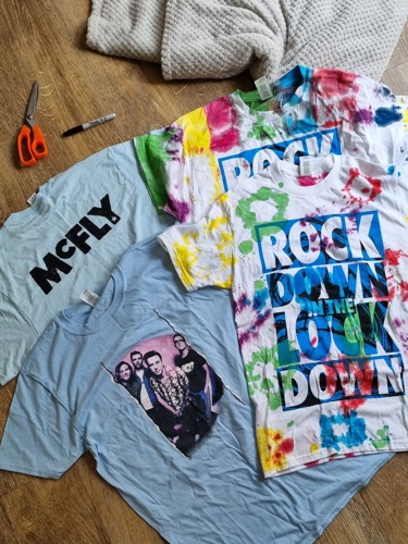 Four McFly t-shirts in assorted colours with scissors and a pen next to them