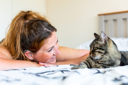 brunette woman lying on bed looking at brown tabby cat