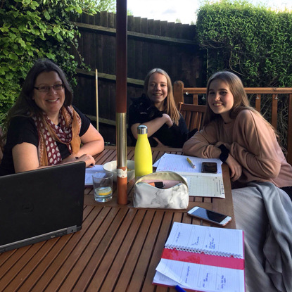 one woman, two young girls and a black cat at a garden table