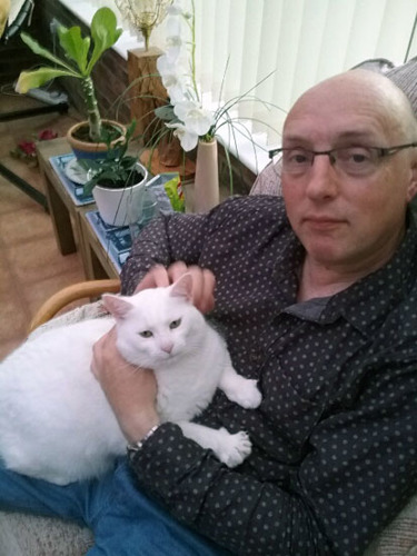 man wearing glasses sitting with white cat on his lap