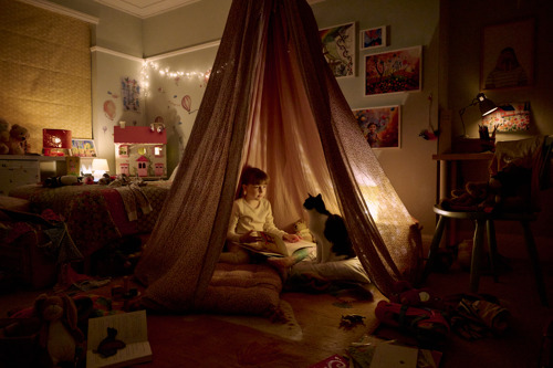 young white girl with brunette hair and black-and-white cat sitting inside a teepee tent in a child's bedroom with fairy lights around them