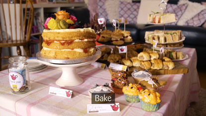 selection of cakes, sandwiches and sausage rolls next to a jar of change
