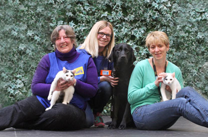 three women with black dog and two white-and-black cats