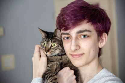 young boy with purple hair holding a tabby cat