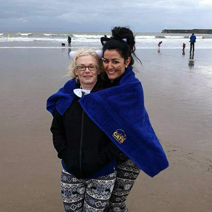 two women wrapped in Cats Protection blanket on the beach