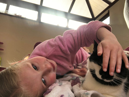 young blonde girl petting black and white cat on the head