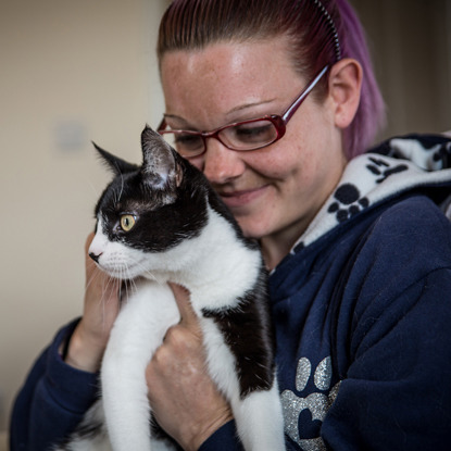 woman with blonde and purple hair hugging black and white cat
