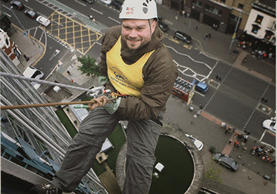 man abseiling down side of building wearing Cats Protection vest