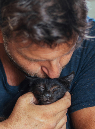 man kissing black kitten on the head