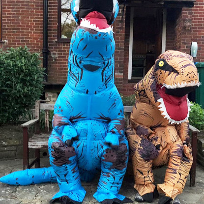 two people in inflatable T-rex dinosaur costumes sitting on bench