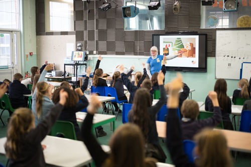 Children in classroom all holding arms up