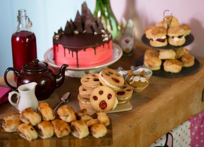 table of afternoon tea: cakes, biscuits, sausage rolls, scones and teapot