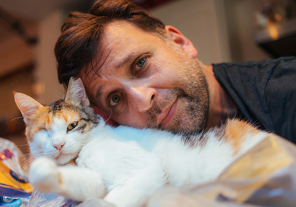 man cuddling tortie and white cat with one eye