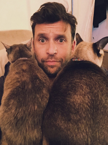 man with two brown cats sitting on his lap