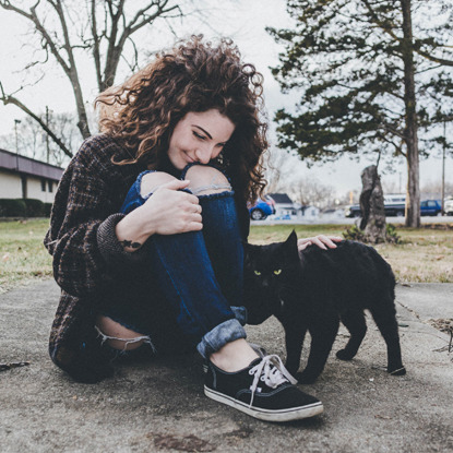 woman sitting outside and stroking black cat