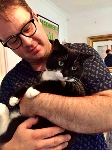 man with glasses holding black and white cat