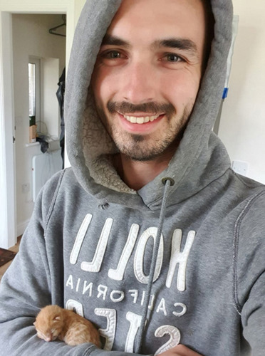 man in grey jumper holding newborn ginger kitten