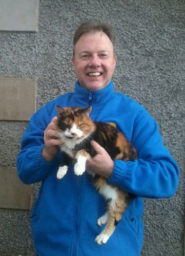 man wearing Cats Protection fleece and holding calico cat