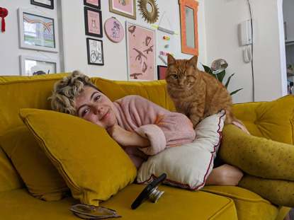 woman lying on yellow sofa with ginger cat sitting on her