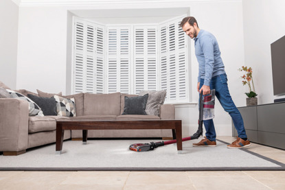 man vacuuming under coffee table with Shark vacuum cleaner