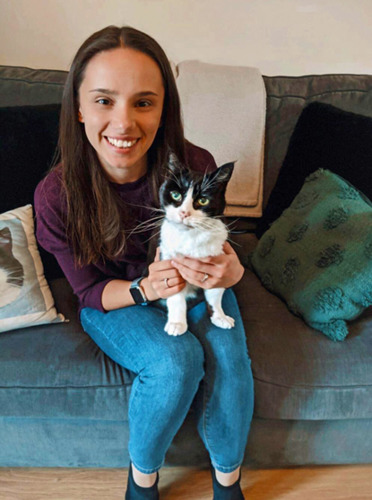 long-haired brunette woman sitting on grey sofa with black-and-white cat on her lap