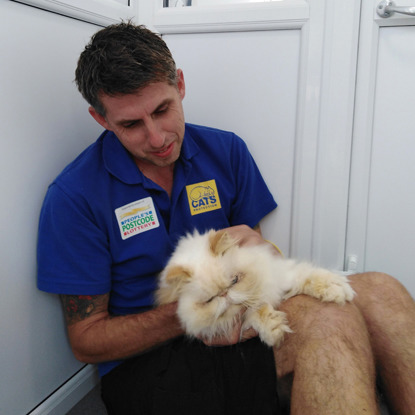 man wearing blue Cats Protection t-shirt with cream-coloured flat-faced cat on lap