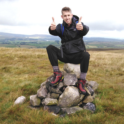 man sitting on pile of rocks on top of hill and giving two thumbs up