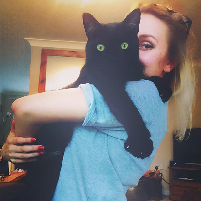 blonde woman in blue t-short holding black cat over shoulder