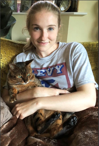 young blonde woman sitting on sofa cuddling brown tabby cat