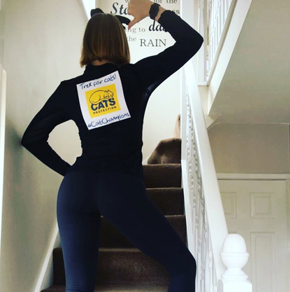 Woman on staircase with her back to camera pointing at Cats Protection logo on the back of her top