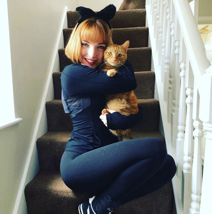 redhead woman dressed as black cat holding ginger cat on staircase