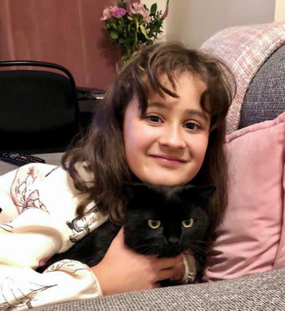 young brunette girl cuddling black cat on sofa