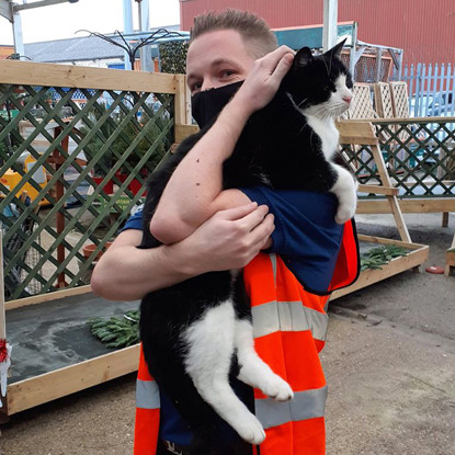 Short-haired brunette man wearing orange high-vis jacket holding black-and-white cat